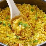 A variety of dishes paired with yellow rice, including grilled shrimp, roasted vegetables, and a chicken curry.